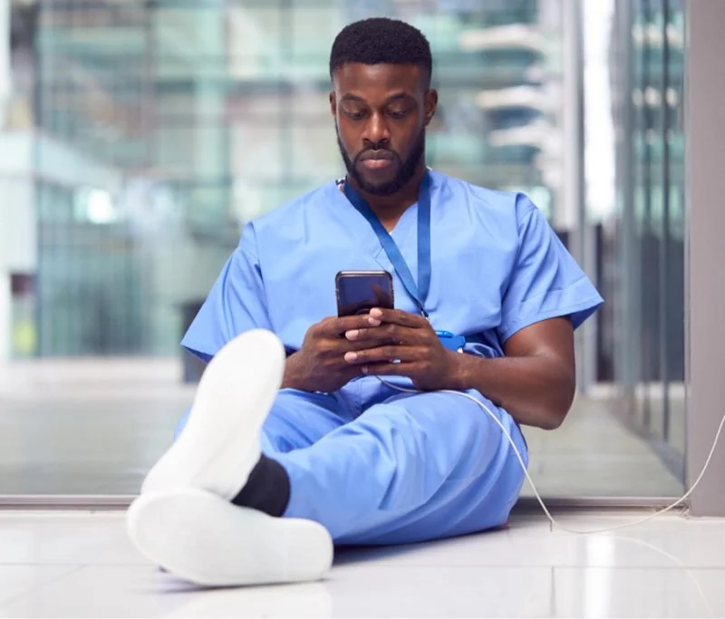 A nurse sitting on the floor and looking at a phone
